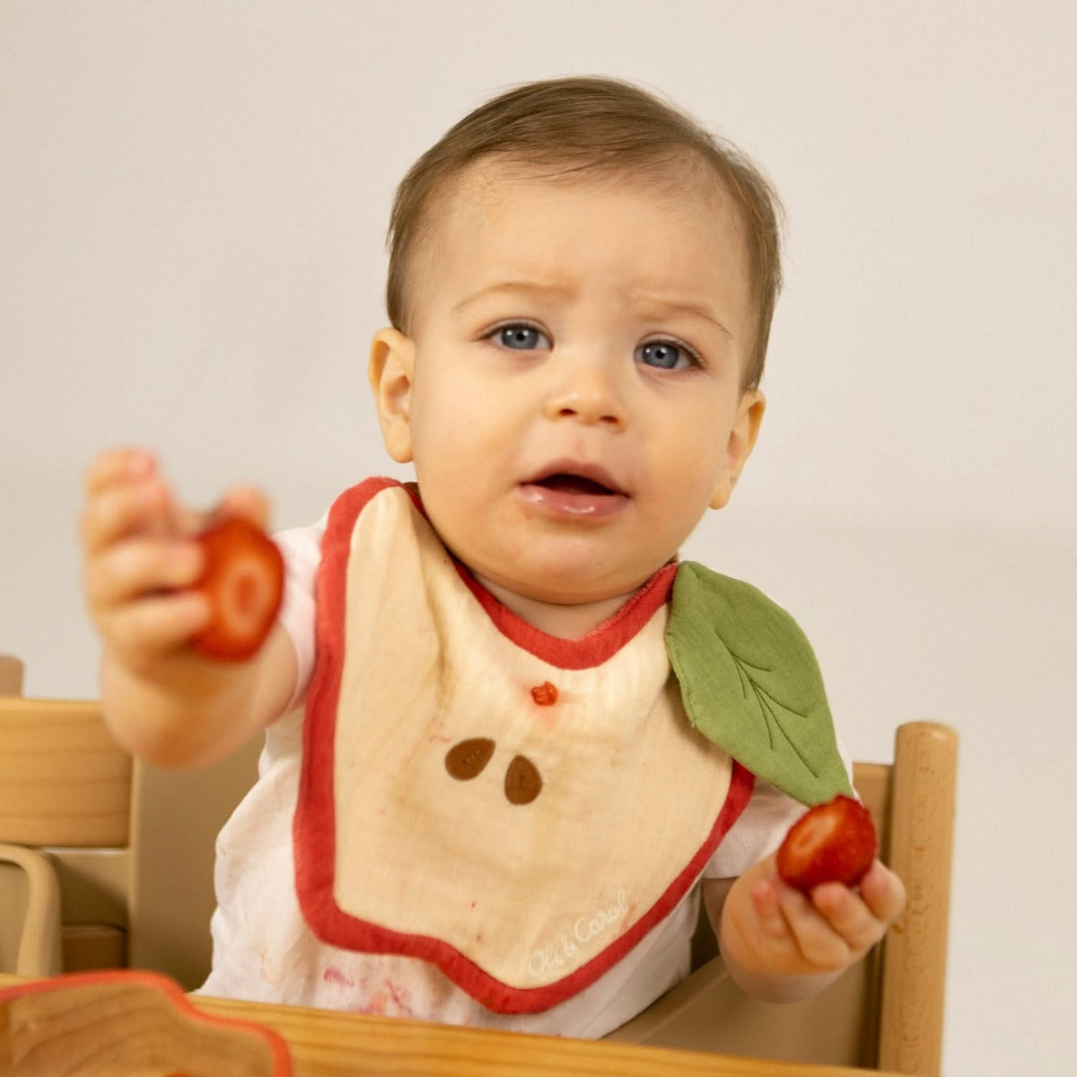 Bebé na cadeira da refeição com o babete em forma de maçã Oli & Carol | oli-carol-babete-maca-lollakids