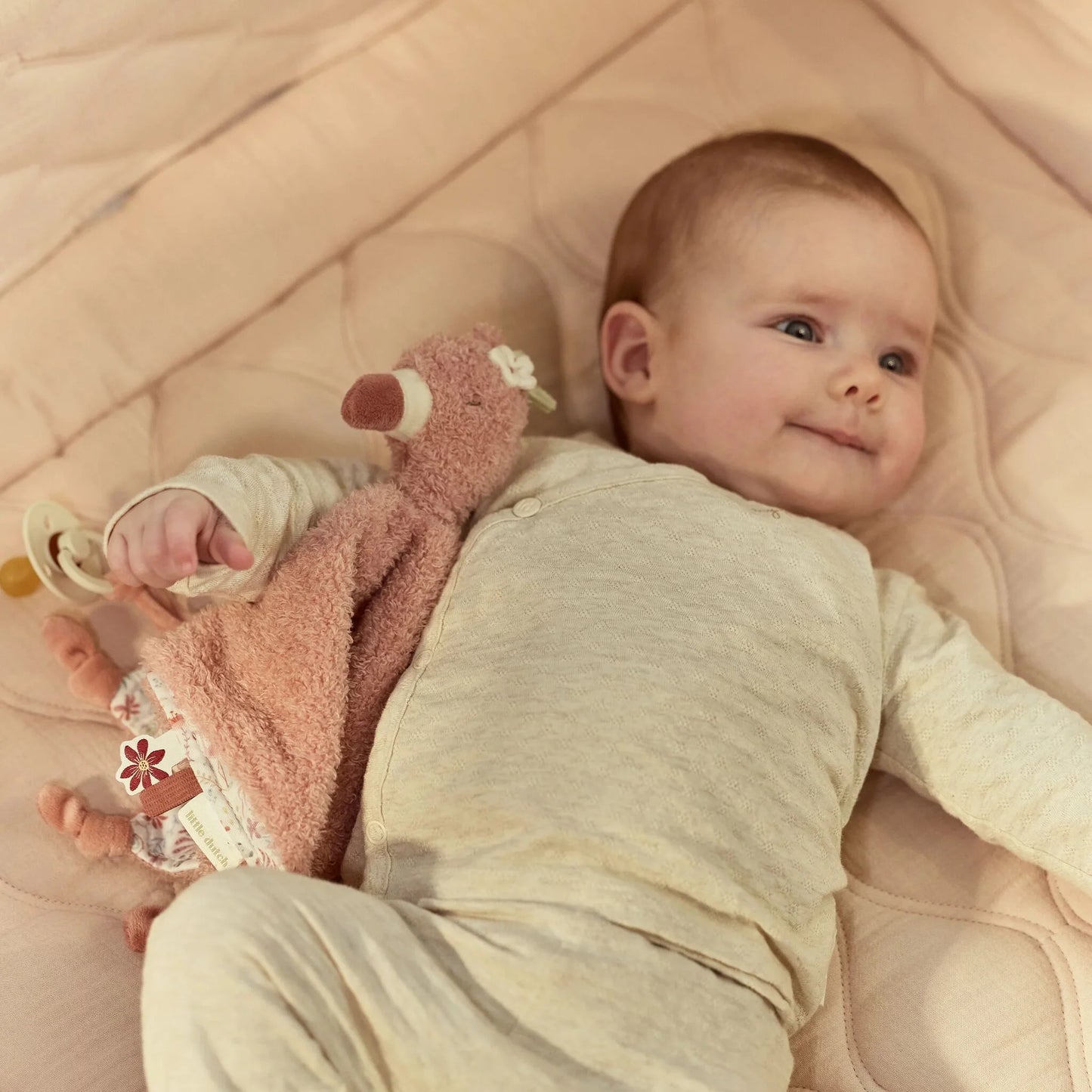 Bebé a sorrir com doudou flamingo rosa